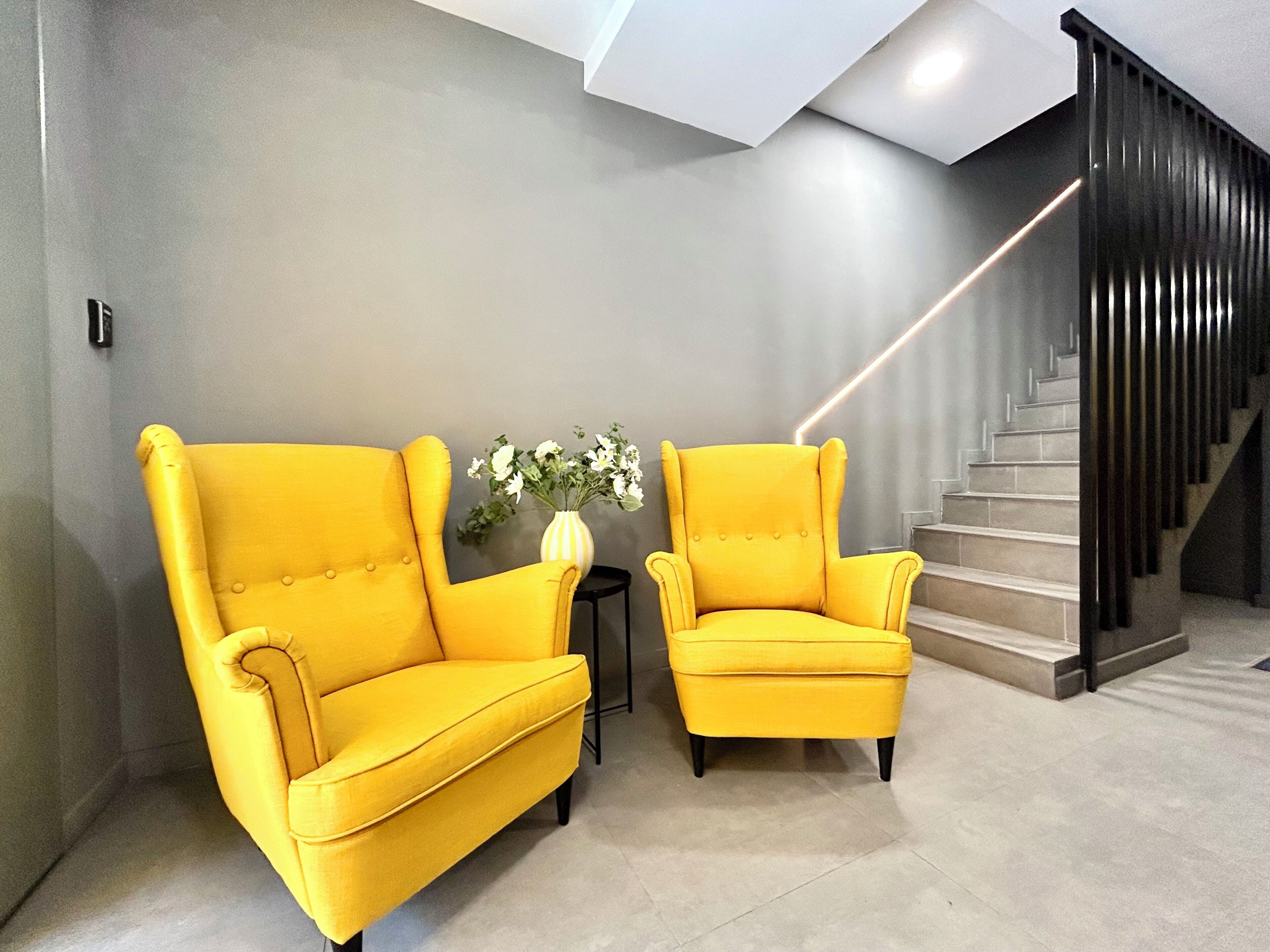 A modern interior with two yellow armchairs, a vase with flowers, and a staircase.