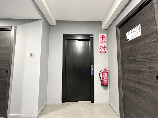 A hallway with a black elevator door, a fire extinguisher, and a sign indicating no smoking. - ZUR Boutique Hostel (Fuengirola)