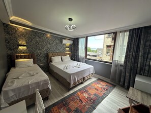 Habitación de hotel con dos camas, un tapete estampado y vistas a edificios a través del ventanal.