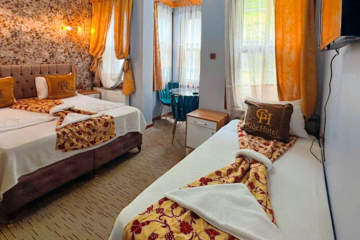 A hotel room with two beds, a wooden ceiling, floral wallpaper, and a small table.