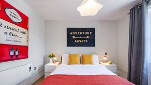 A hotel room with a large bed, two bedside tables with lamps, a red textured rug, a wall with a map and text, and a window with curtains.