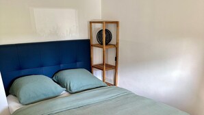 A bedroom with a bed, a blue headboard, a wooden shelf with a round object, and a woven rug. - Apartment Zephyr - 1 minute from the sea (Cagnes-sur-Mer)