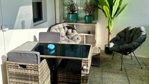 A small patio area with a glass-top table, wicker chairs, a black lounge chair, and potted plants. - Apartment Zephyr - 1 minute from the sea (Cagnes-sur-Mer)