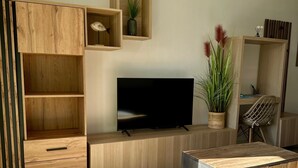 A modern living room with a flat-screen TV, wooden furniture, and a potted plant. - Apartment Zephyr - 1 minute from the sea (Cagnes-sur-Mer)