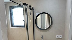 A modern bathroom with a glass shower enclosure, a white sink, a round mirror, and a towel rack. - Apartment Zephyr - 1 minute from the sea (Cagnes-sur-Mer)