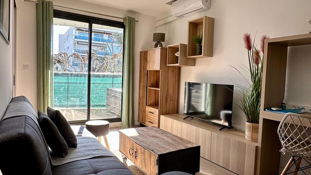 A modern living room with a sofa, TV, wooden cabinets, and a view of the outside. - Apartment Zephyr - 1 minute from the sea (Cagnes-sur-Mer)
