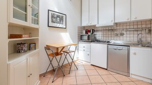 Una cocina compacta con armarios blancos, microondas, hervidor y lavavajillas.