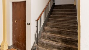 Una escalera con barandilla de madera y pasamanos metálico, que conduce a un rellano con una puerta y un ventanal con reja.