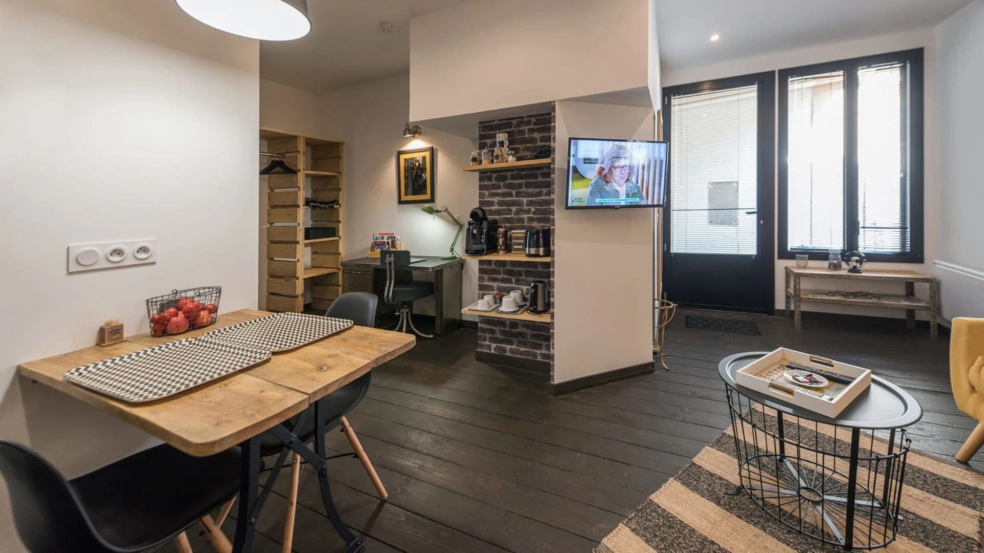 A compact living space with a dining area, kitchenette, and a TV mounted on the wall.