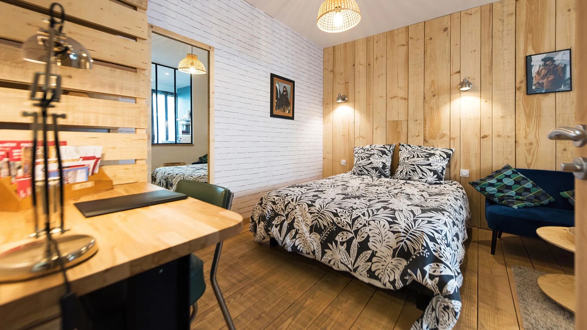 A cozy bedroom with a bed, a desk, and a chair. There is a wooden wall and a window.
