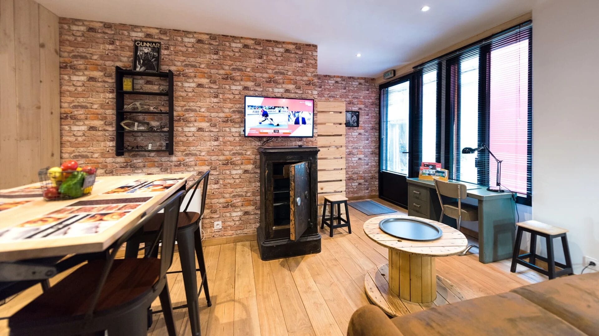 A modern living room with a brick wall, a television, a fireplace, and a dining area with a table and chairs.