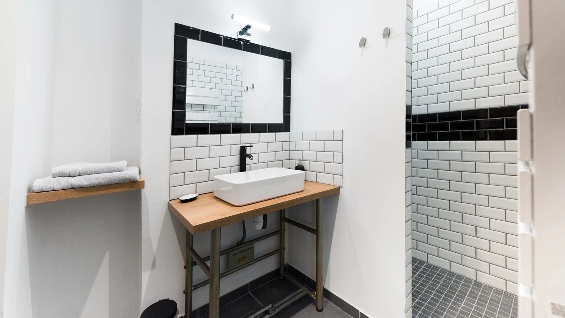 A modern bathroom with a white sink, black and white tiled walls, and a wooden countertop.