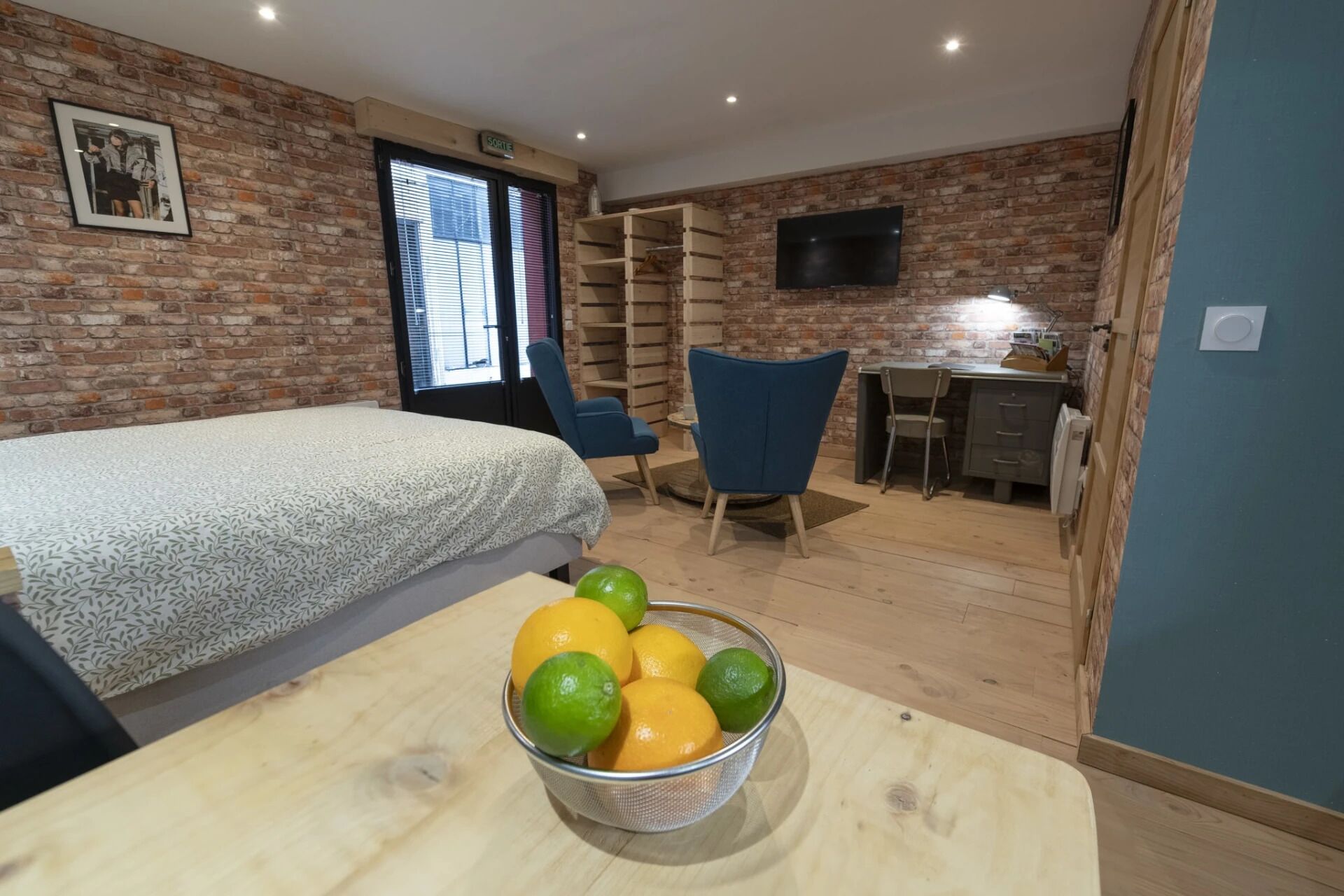 Une pièce comprenant un lit, un bureau, une chaise et un saladier de fruits posé sur une table.
