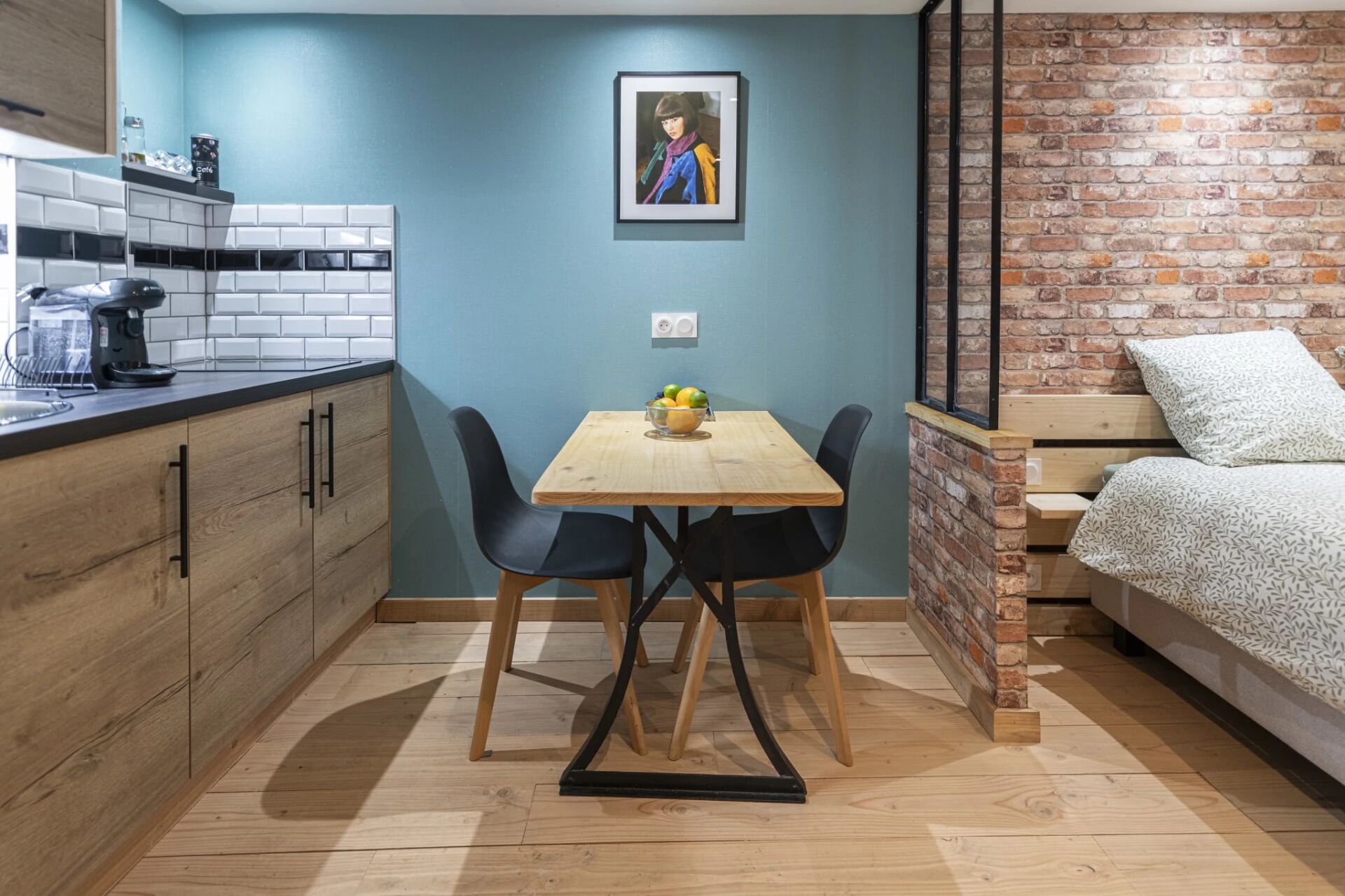 Una cocina compacta con cafetera, una mesa de comedor y dos sillas, y una pared de ladrillo.