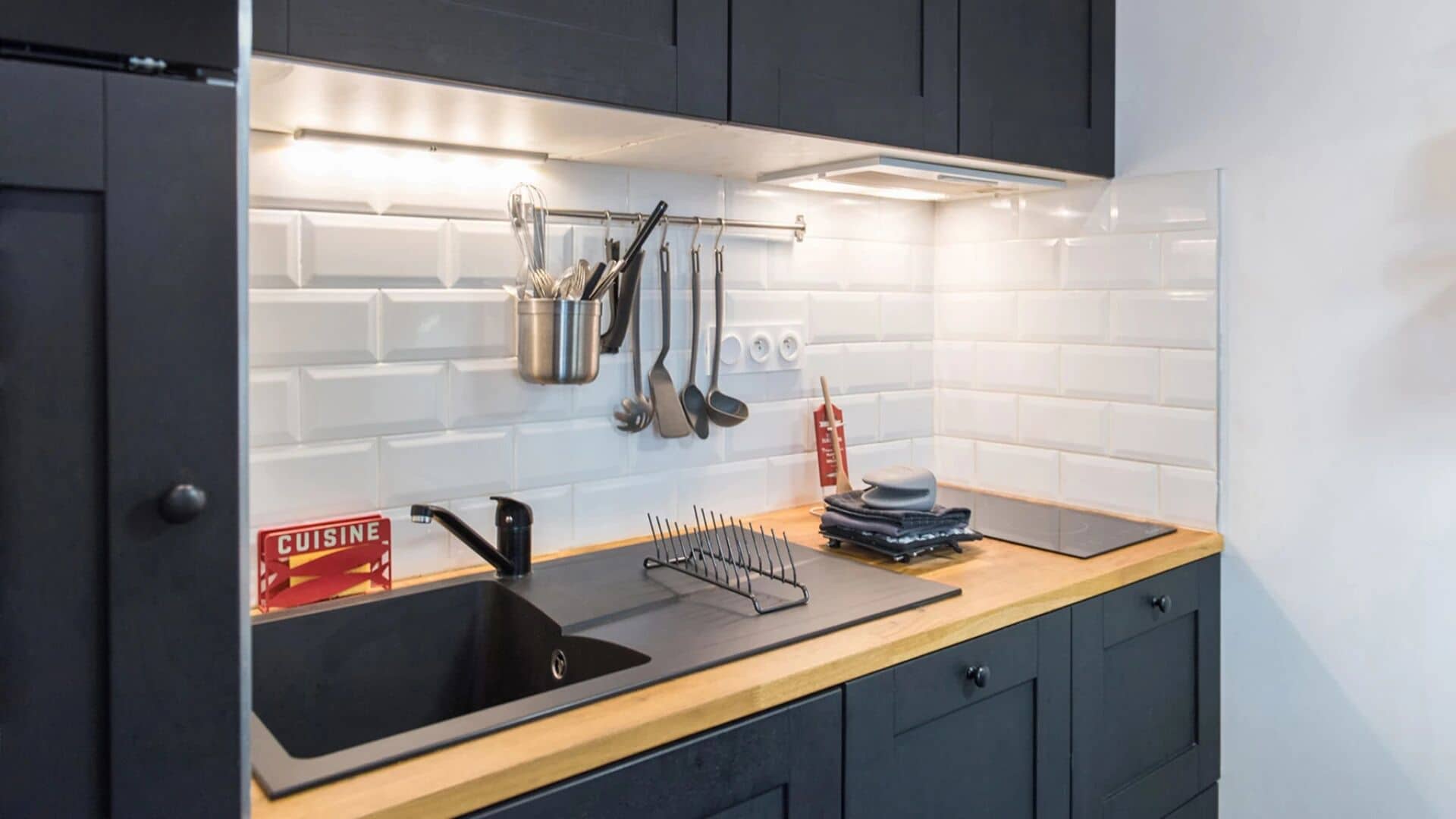 Una cocina moderna con encimera negra, un lavamanos y un soporte para utensilios.
