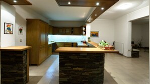 A modern kitchen with wooden cabinets, a central island, and pendant lighting. - Escape Villa in Melissochori (Oraiokastro)