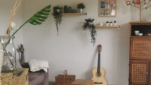 En stue med sofa, guitar, et pyntetræ, et farverigt tæppe og et skab med planter.