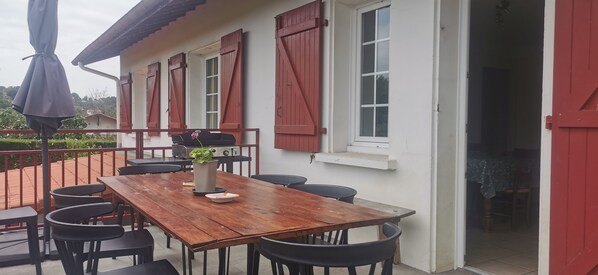 A wooden table with chairs, a potted plant, and a small table with a plate and a candle. - Basque-style house near Bayonne, Anglet, and Biarritz (st pierre d'irube)