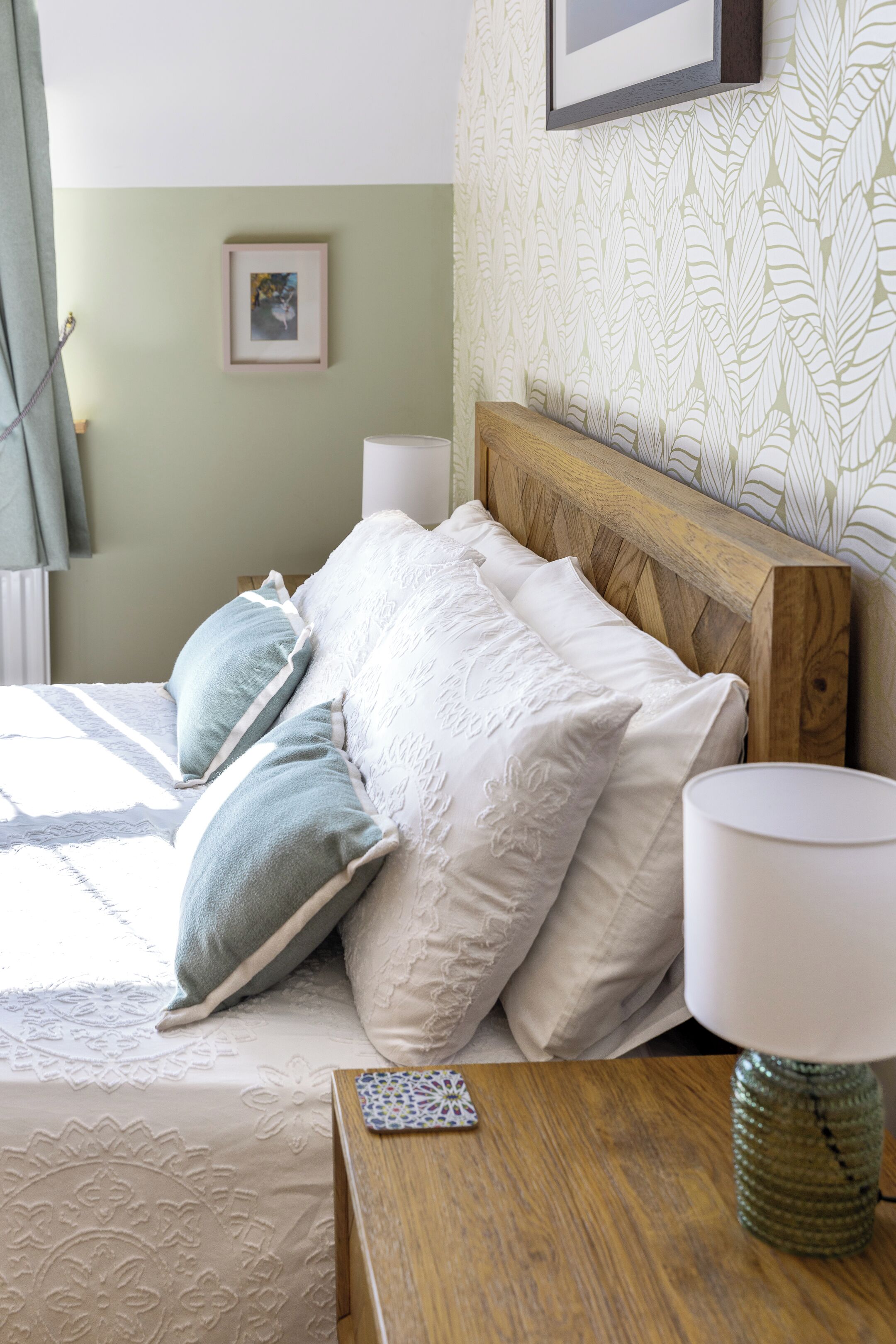 A neatly made bed with pillows, a bedside table with a lamp, and a framed picture on the wall.