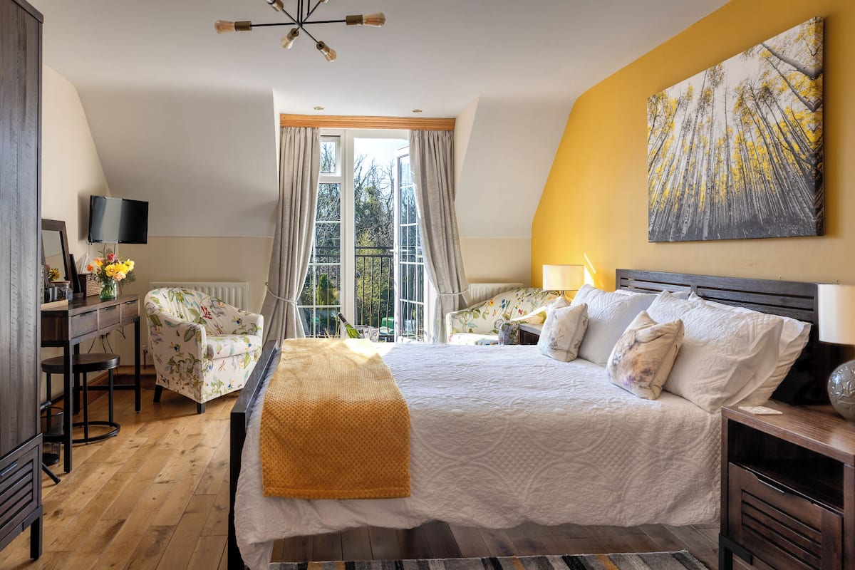 Een slaapkamer met een groot bed, een stoel, een bureau, een televisie en een raam met gordijnen.