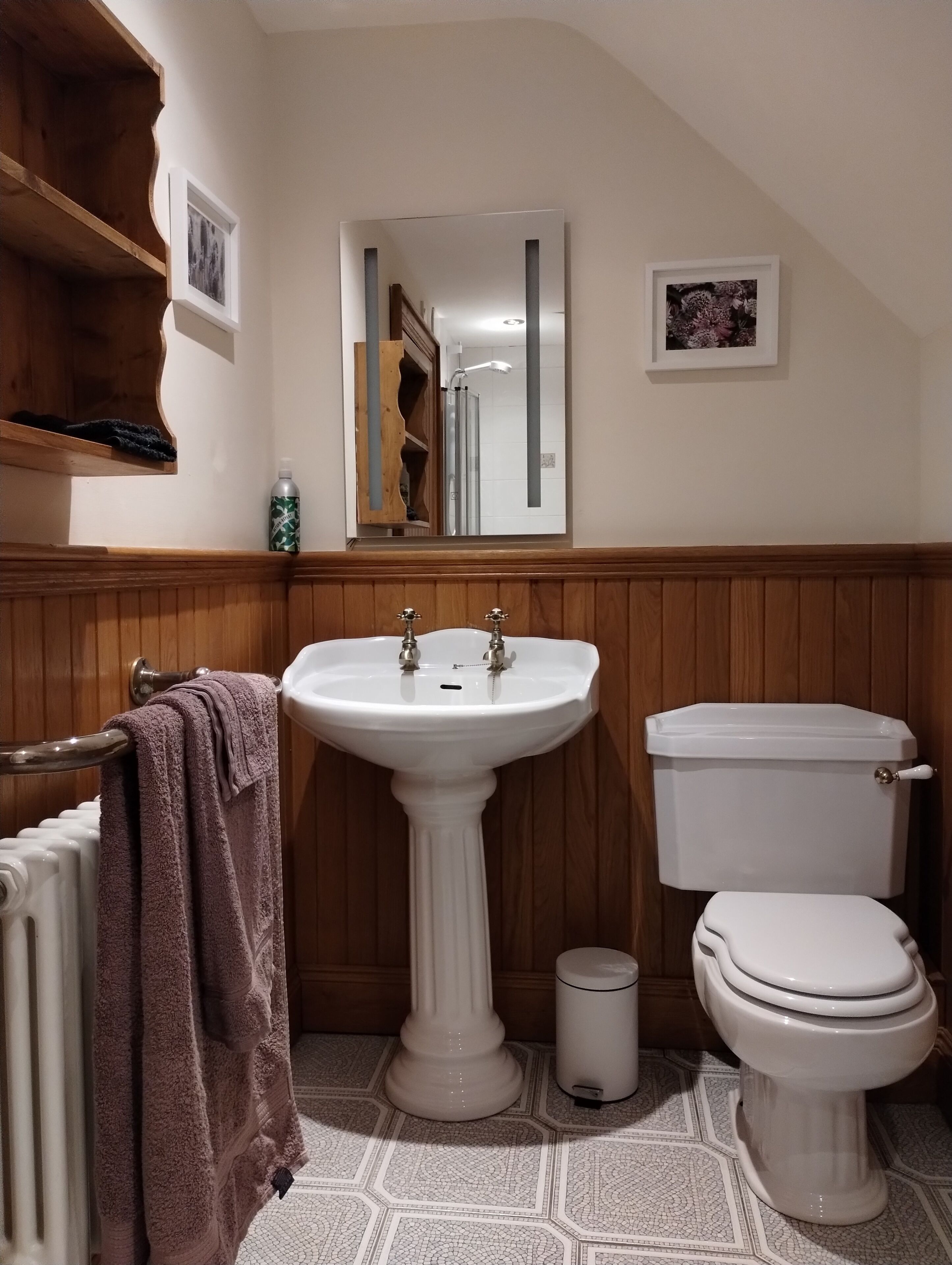 A bathroom with a pedestal sink, toilet, radiator, and wooden paneling.