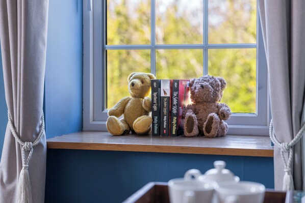 A window with a view of trees, a shelf with books and two teddy bears, and a white tray with teacups. - Rossclare Lodge (Enniskillen)