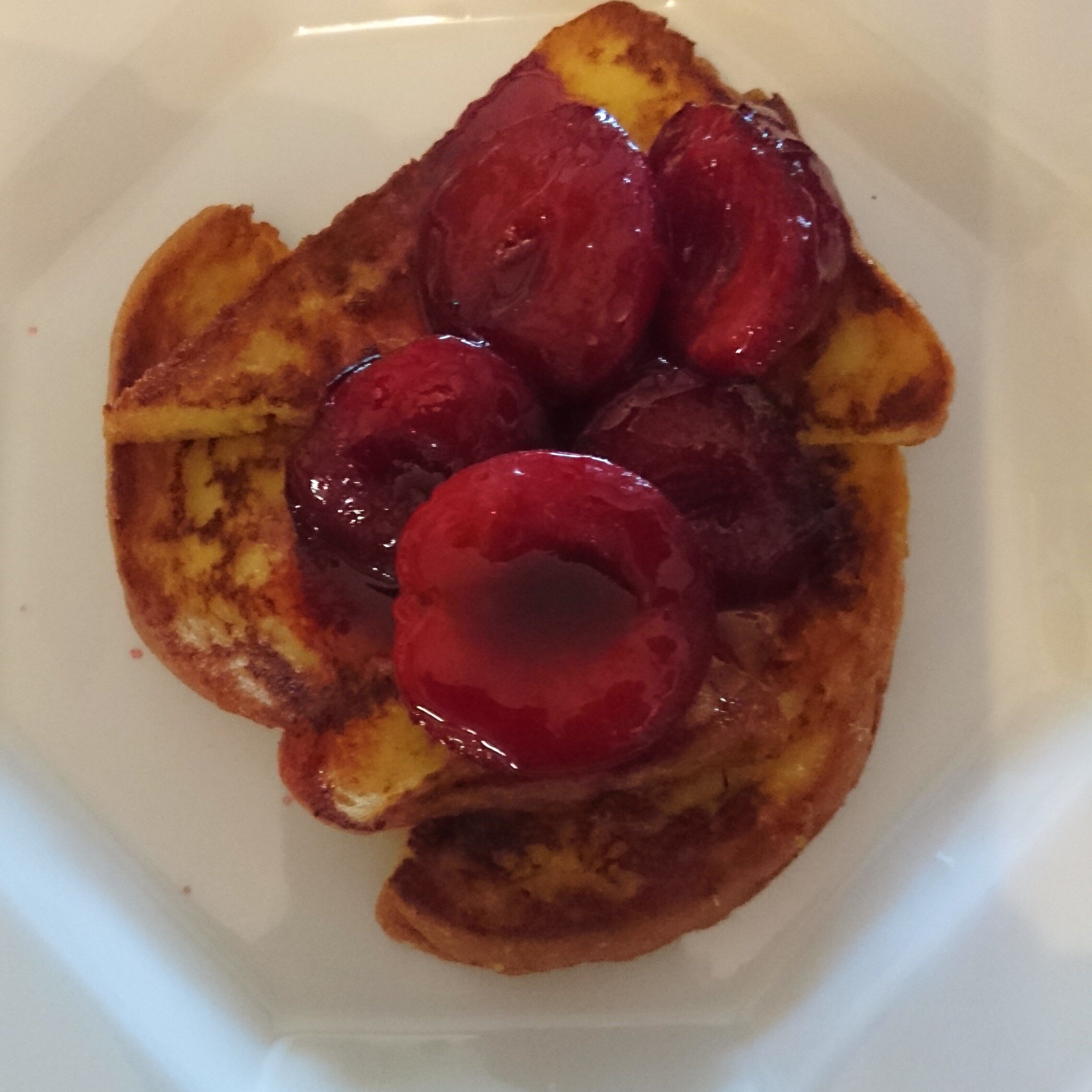 A plate with a slice of toast topped with a red sauce and a cherry.
