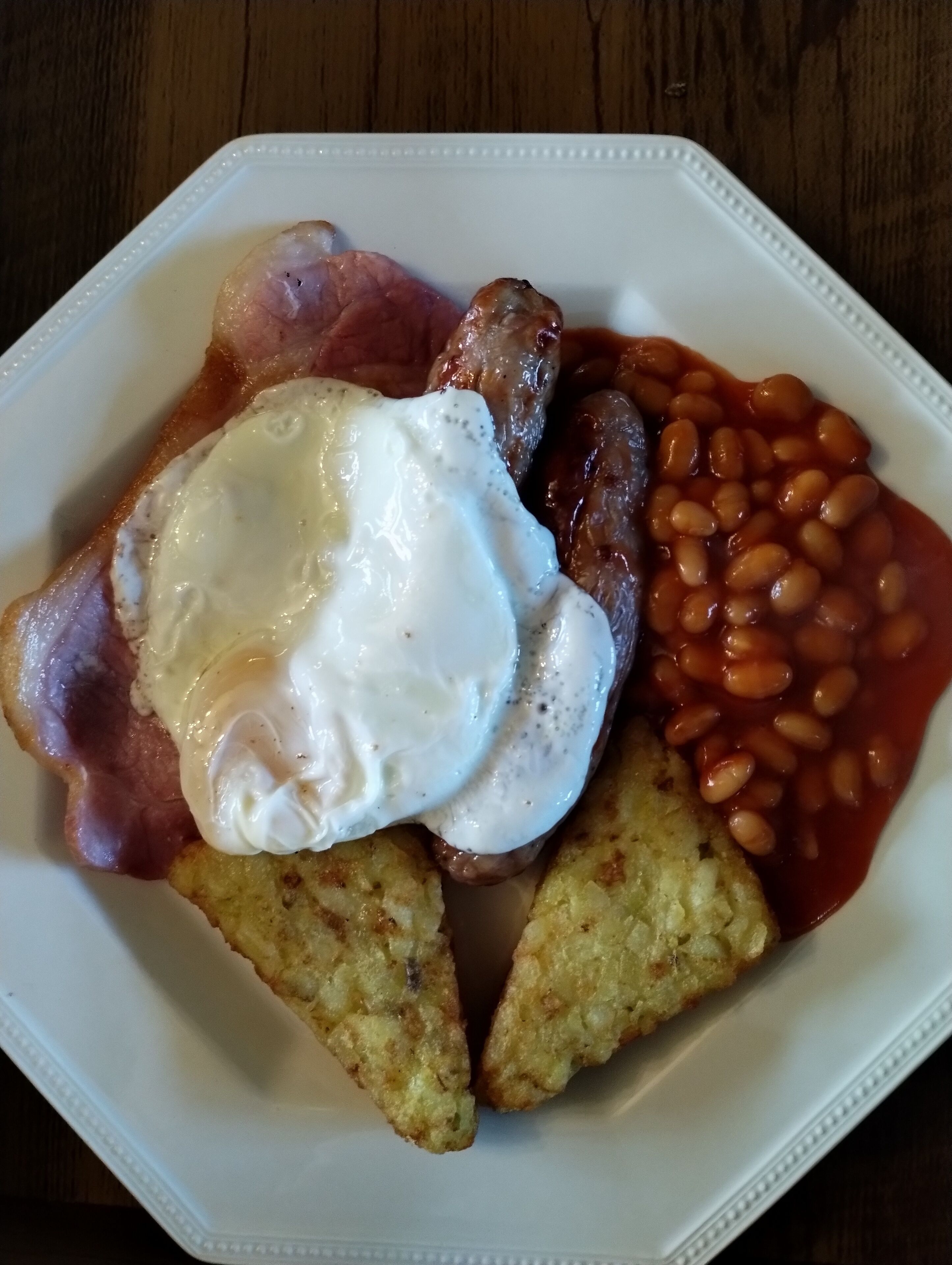 Une assiette blanche contenant un petit-déjeuner composé d’œufs, de bacon, de haricots et de pain grillé.