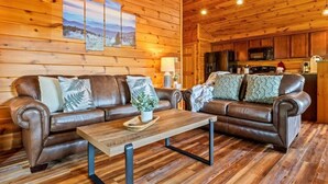 Interno di una baita in legno con un divano in pelle, un tavolino in legno e una zona cucina.