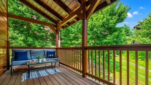 Un terrazzo in legno con divano e tavolo, circondato da una ringhiera, con vista su un paesaggio verde e rigoglioso.