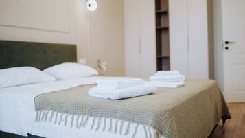 A neatly made bed with white linens and a beige throw blanket, a wall-mounted light fixture, and a door to a closet.