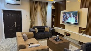 A modern living room with a large flat-screen TV, a dark sofa, a light-colored sofa, and a coffee table. - Ivorian Heaven Home (FCT)