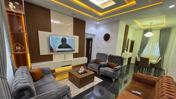 A modern living room with a flat-screen TV, grey and brown sofas, a coffee table, and a glass dining table. - Ivorian Heaven Home (FCT)