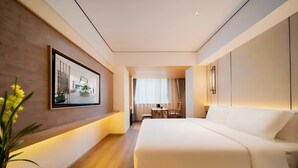 Habitación de hotel moderna con una cama grande, un escritorio con silla, una planta en maceta y un cuadro enmarcado en la pared.