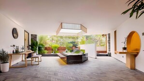 Un interior moderno con una zona de estar central, un suelo con estampado de espiga y un gran ventanal con vistas a un jardín.