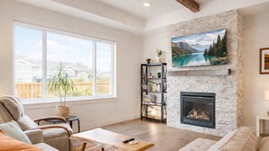 Uma sala de estar com lareira, estante de livros e uma grande janela com vista para casas.