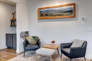 A living room with a painting, a bookshelf, a cabinet, two chairs, a small table, and a rug.