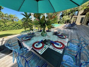 An outdoor dining area with a table set for four, surrounded by blue chairs, under a green umbrella. - Rose Hall (Montego Bay)