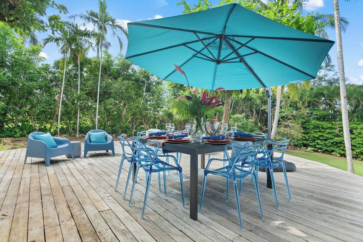A wooden deck with a table set for dining, surrounded by blue chairs and a large turquoise umbrella.