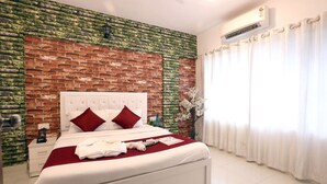 A bedroom with a brick-patterned wall, a white bed with red pillows, a white nightstand, and a white air conditioning unit. - 1 BHK Private Suite ( Gagal Home) (Mumbai)