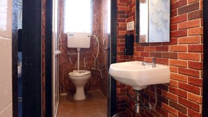 A bathroom with a toilet, sink, and a mirror on a brick wall. - 1 BHK Private Suite ( Gagal Home) (Mumbai)