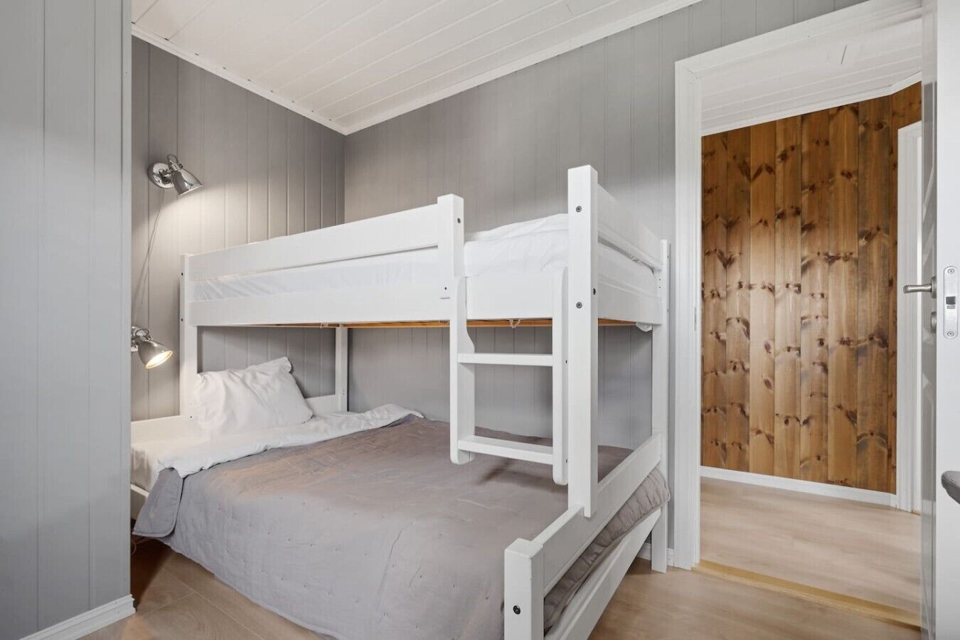 Een slaapkamer met een stapelbed, bureau en lamp, een houten deur en lichte wanden.