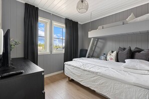 A bedroom with a bunk bed, a desk with a computer and remote, and a window with curtains.