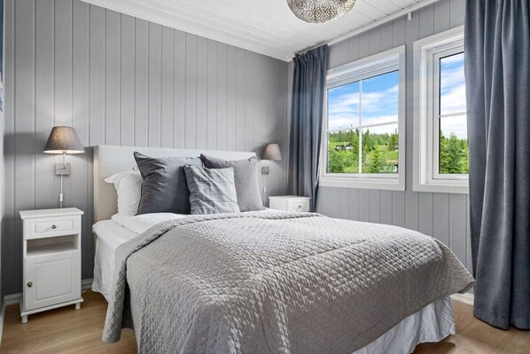 Un dormitorio con cama, dos mesitas de noche, una ventana con cortinas y vistas al exterior.