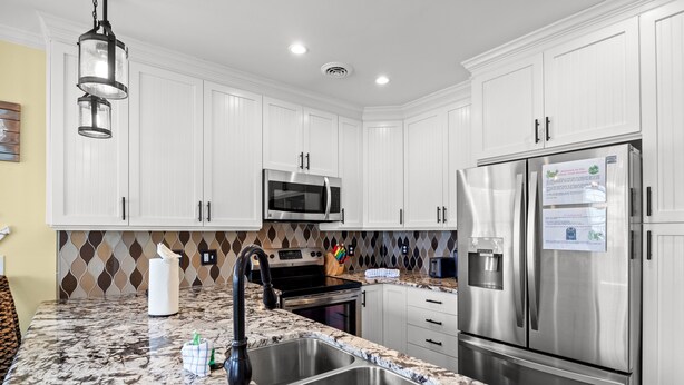 A modern kitchen with white cabinets, stainless steel appliances, a granite countertop, and a patterned backsplash.