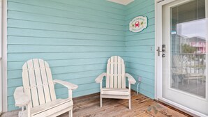 A corner of a building with turquoise siding, two white Adirondack chairs, and a door with a glass panel.