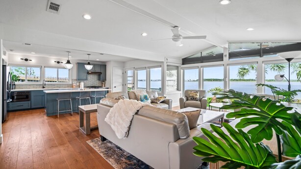 A spacious living area with a large sofa, a dining table, and a kitchen area with a bar. - Relax in Style  – 5BR Home w/ Pool, Hot Tub & Stunning Harbor Views (Galveston)