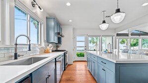 A modern kitchen with a central island, a double sink, and a view to the outdoors. - Relax in Style – 5BR Home w/ Pool, Hot Tub & Stunning Harbor Views (Galveston)