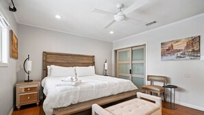 A bedroom with a wooden bed, a nightstand, a bench, a chair, and a painting on the wall. - Relax in Style – 5BR Home w/ Pool, Hot Tub & Stunning Harbor Views (Galveston)