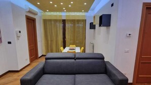 A room with a sofa, a dining table with chairs, and a large window with curtains. - Cozy and Comfortable Apartment near Fiumicino Airport (Lazio)